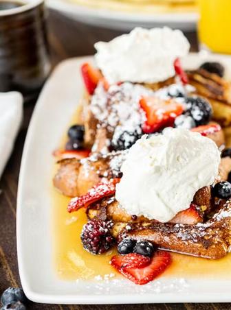 French toast topped with fresh berries and whipped cream on a white plate