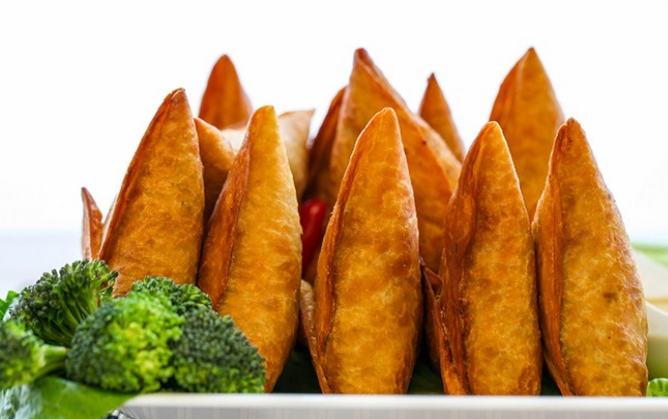Crispy golden sambusa pastries on a plate with fresh broccoli at Biftu African Market