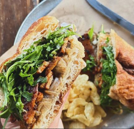A sandwich piled with arugula and meat next to potato chips at Bread &amp; Circus Kitchen