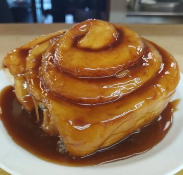 A jumbo caramel roll with glossy caramel topping on a white plate at The Crack'd Pot