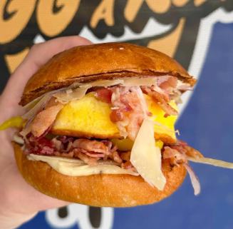 A hand holding a bacon and egg breakfast sandwich on a toasted roll from Egg On A Roll