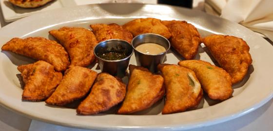 A plate of golden fried empanadas with dipping sauces