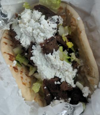 A gyro wrap topped with crumbled white cheese, lettuce and meat, wrapped in foil at Gyro Time
