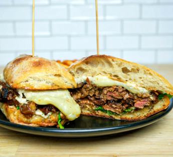 Two grilled sandwiches with melted cheese and steak on a black plate at Look's Marketplace