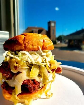 A tall loaded burger with shredded cabbage and sauce on a white plate at Murph's Burgers
