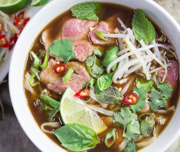 A bowl of pho with sliced beef, fresh herbs, bean sprouts and lime at Pho Thai