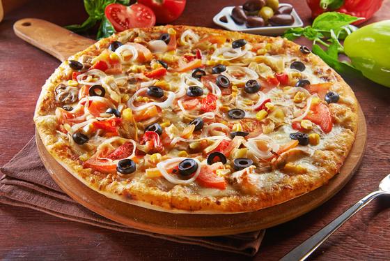 A loaded pizza with peppers and olives on a wooden serving board