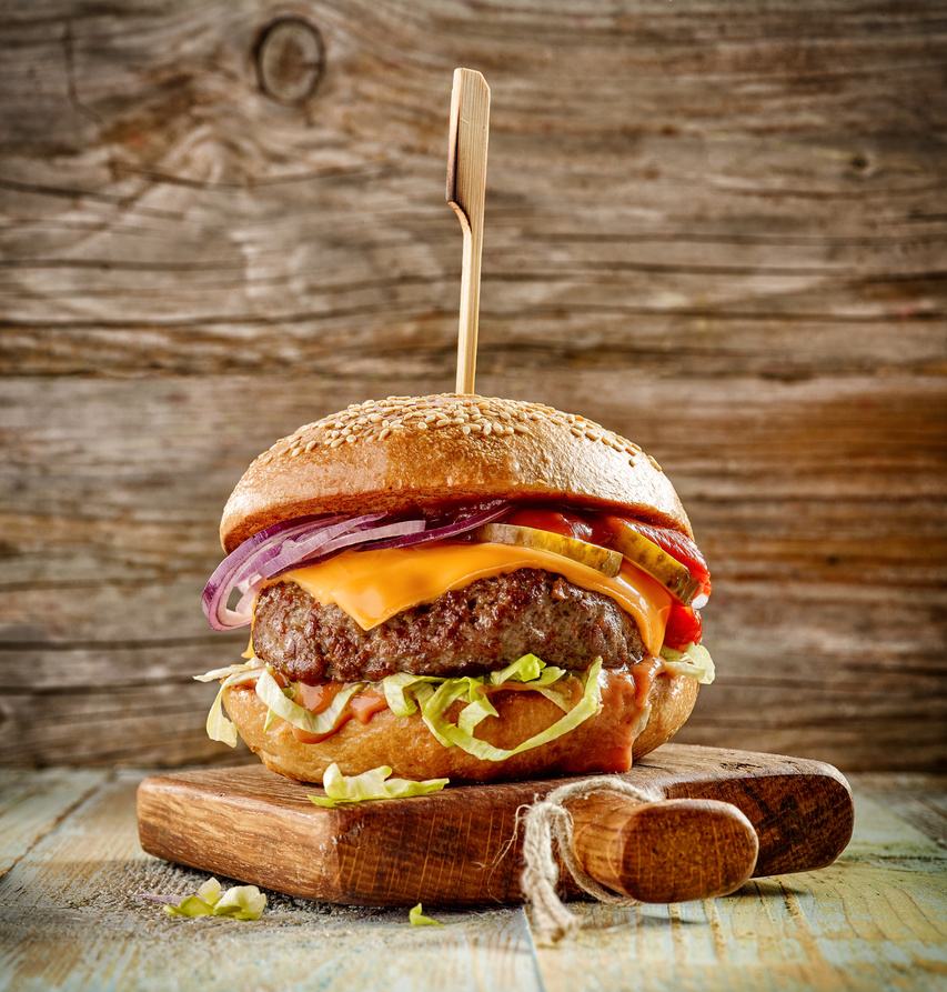 A stacked wagyu burger with melted cheese on a wooden board